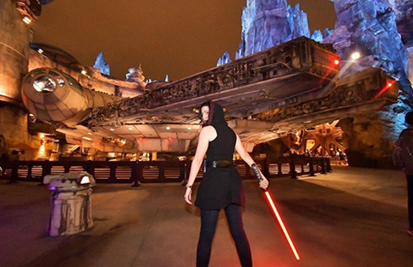 Girl in Sith hooded Disneybound with lightsaber in front of FAlcon